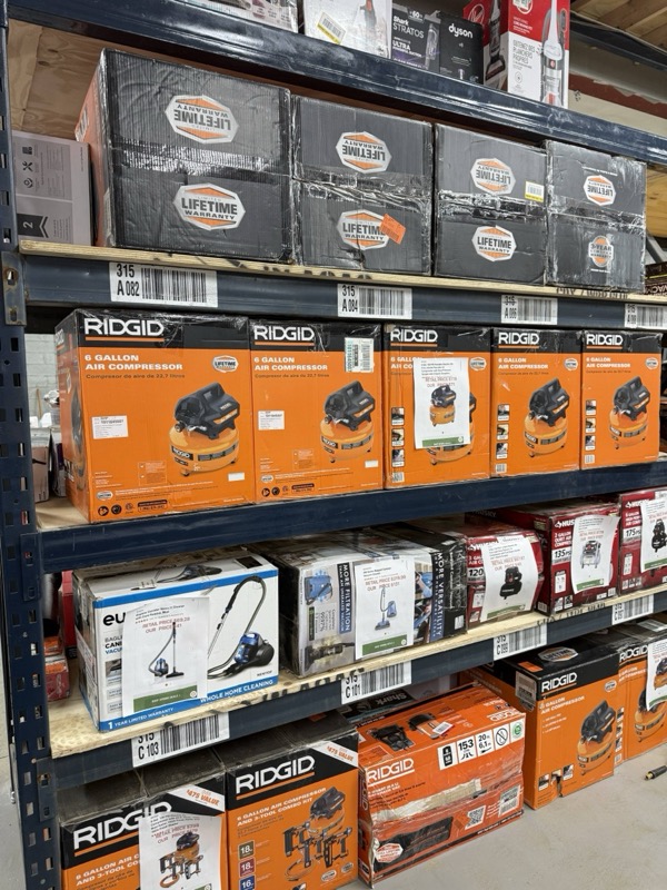 Ridgid 6-gallon air compressors stacked on warehouse shelving with Lifetime products above